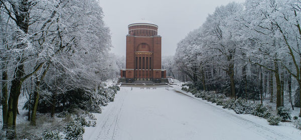 Snow covered trees by building against sky