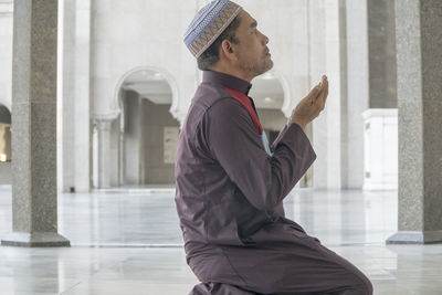 Side view of mature man praying while kneeling at mosque