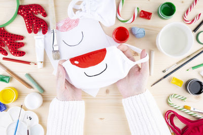 High angle view of woman hands holding mask by various objects over table