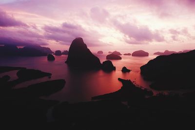 Silhouette rocks in sea against sky during sunset