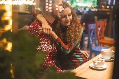 Loving couple in a cafe hug and drink cocoa. photo from the street. reflection of lights 