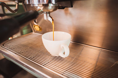 Close-up of coffee machine pouring latte in cup at cafe