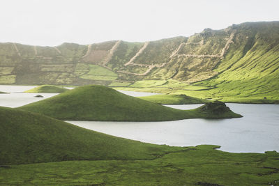 Idyllic view of lake amidst green hills on sunny day
