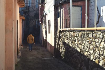 Rear view of man walking on footpath amidst buildings