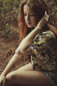 Young woman looking down while sitting on land