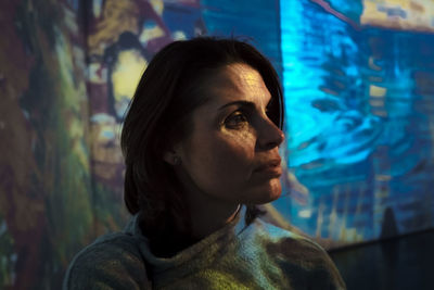 Close-up of thoughtful woman against wall at night