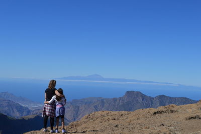 Mother and daughter standing on mountain against clear blue sky