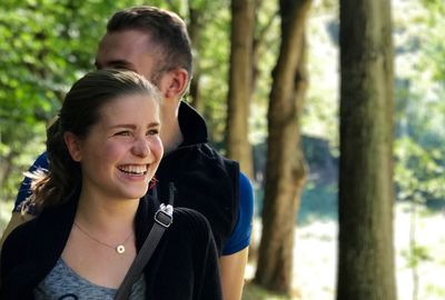 Smiling woman with man looking away against trees