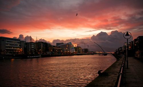 River liffey by buildings in city against cloudy sky during sunset