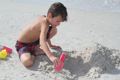 Side view of boy playing with sand at beach