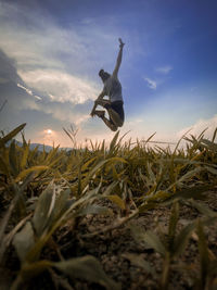 Man jumping on field against sky during sunset