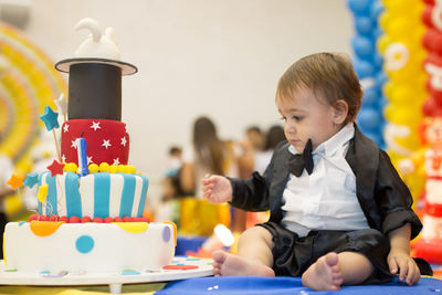 Close-up of cute baby boy sitting birthday cake on table