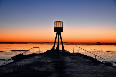 Silhouette lifeguard hut on beach against sky during sunset