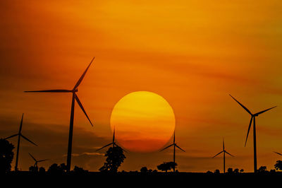 Silhouette wind turbines on field against orange sky