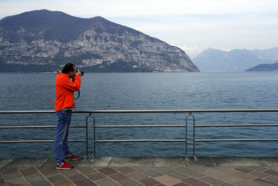 Rear view of man standing by railing against sea
