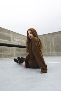 Young woman sitting on retaining wall against clear sky