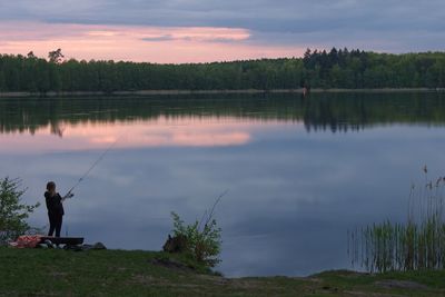 Man fishing in lake against sky