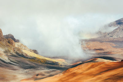 Clouds gather over haleakala national park with red dirt and craters.