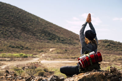 Rear view of man sitting on mountain against sky