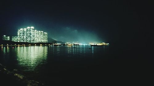 Illuminated city by sea against sky at night