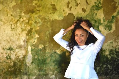 Portrait of smiling beautiful woman with hand in hair against old wall