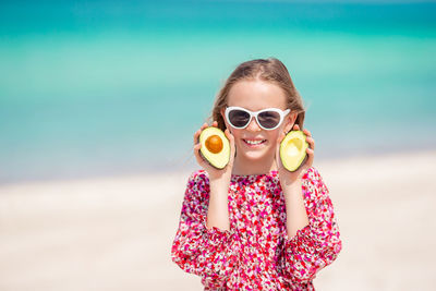 Portrait of smiling girl wearing sunglasses holding avocados