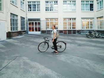Full length of woman with bicycle standing against building