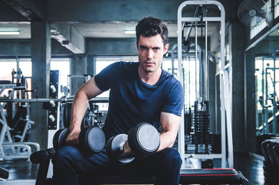 Portrait of young man exercising with dumbbell in gym