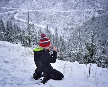 Rear view of boy using mobile phone while kneeling on snow covered field