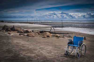 Wheelchair on beach against cloudy sky