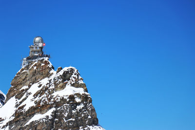 Low angle view of snowcapped mountain against clear blue sky