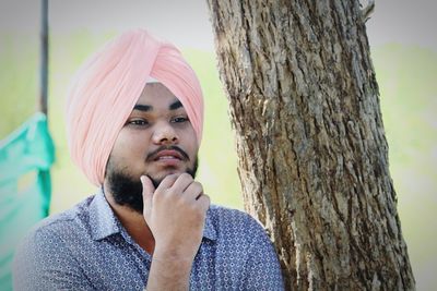 Portrait of young man looking away against tree trunk