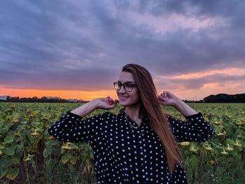 Portrait of smiling young woman standing on field against sky during sunset