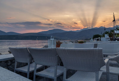 Chairs and table by sea against sky during sunset