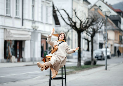 Joyful woman gesturing playfully while seated on a tall chair outside