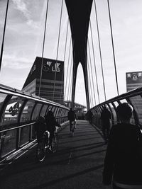 People on suspension bridge against sky in city