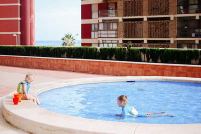 Little boy swimming in pool and little girl playing on board 