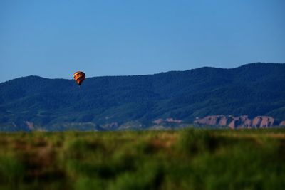 Person paragliding over mountain against clear blue sky