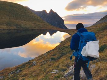 Rear view of hiker by calm lake looking at mountain during sunset