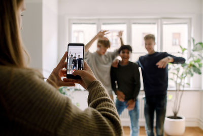 Teenage girl with mobile phone filming male friends dancing in living room