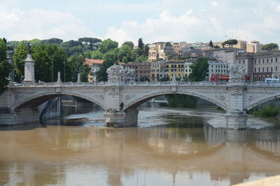 Arch bridge over river by buildings against sky