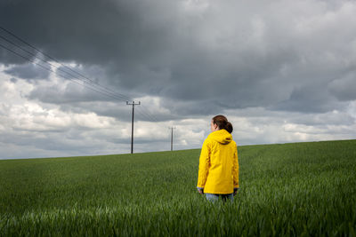 Woman wearing a yellow coat in a green field with a stormy sky background.