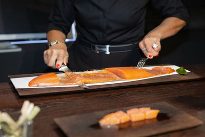 Chef slicing salmon on black wooden table in a restaurant.