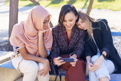 Smiling female friends watching movie in mobile phone