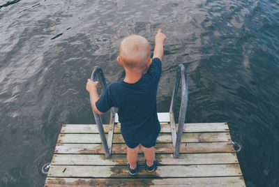 Rear view of man sitting on pier over lake