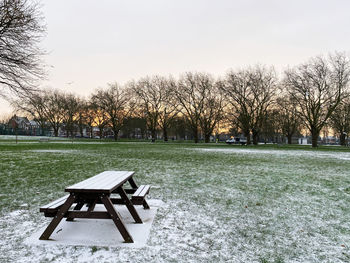 Empty park bench on field against clear sky