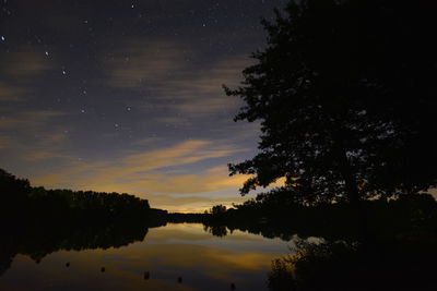 Silhouette trees by lake against sky at night