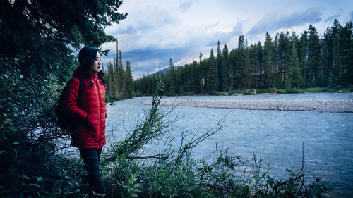 Woman standing by trees in forest against sky