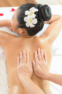 Cropped hands of masseuse giving massage to young woman relaxing at spa