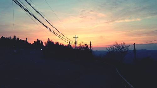 Silhouette electricity pylons against sky during sunset